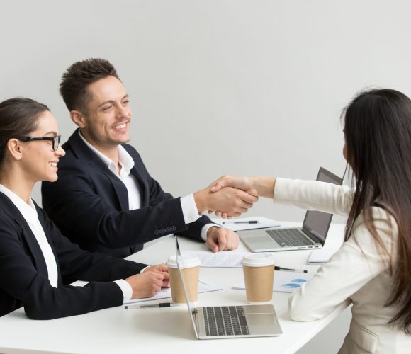 Friendly partners handshaking at group meeting thanking for succ Friendly satisfied partners handshaking at group meeting thanking for successful teamwork, smiling millennial businessman shaking hand greeting businesswoman, respect or making contract deal concept